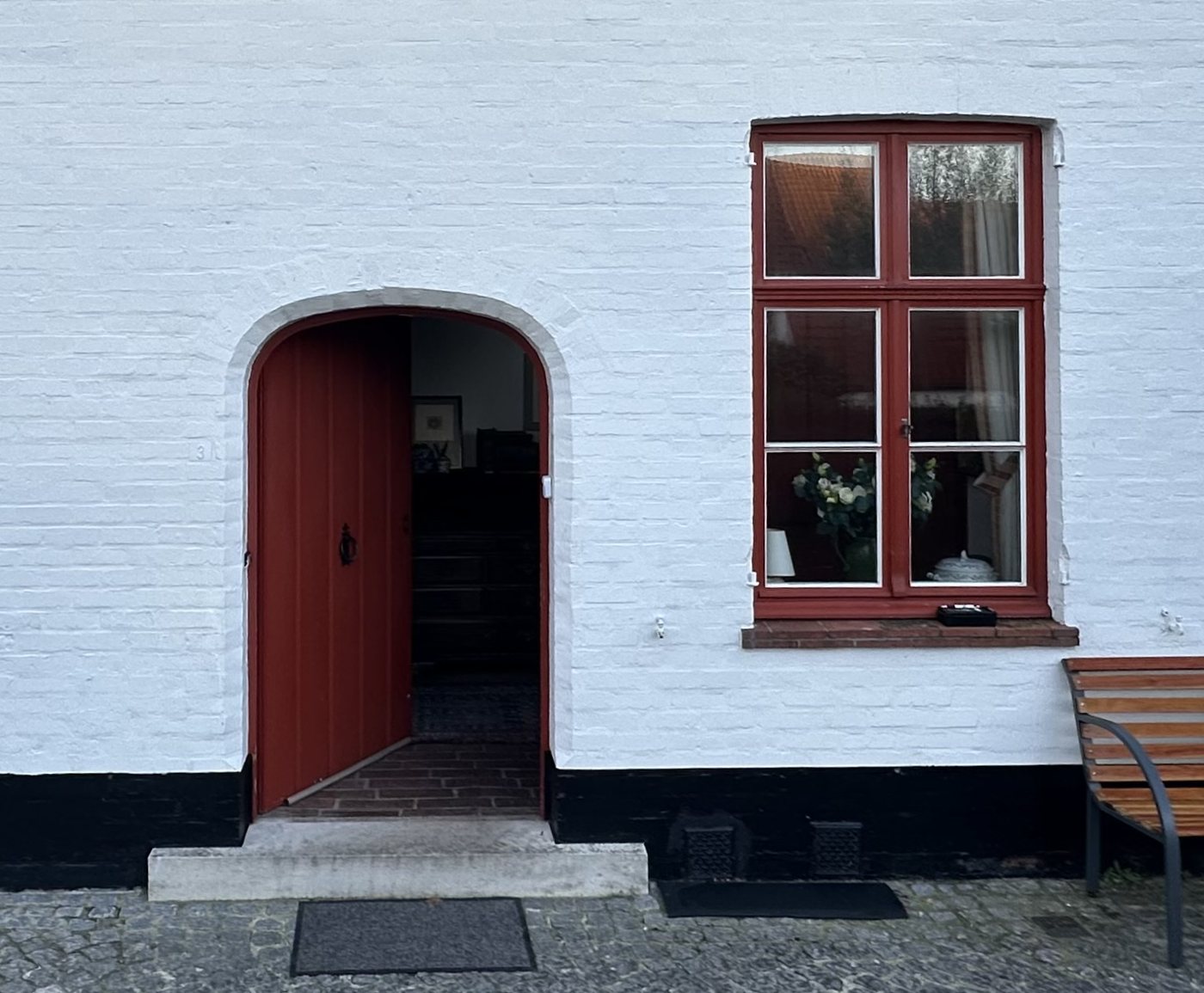 De ingang met gebogen boog, rode deur en een brede stap in witte steen