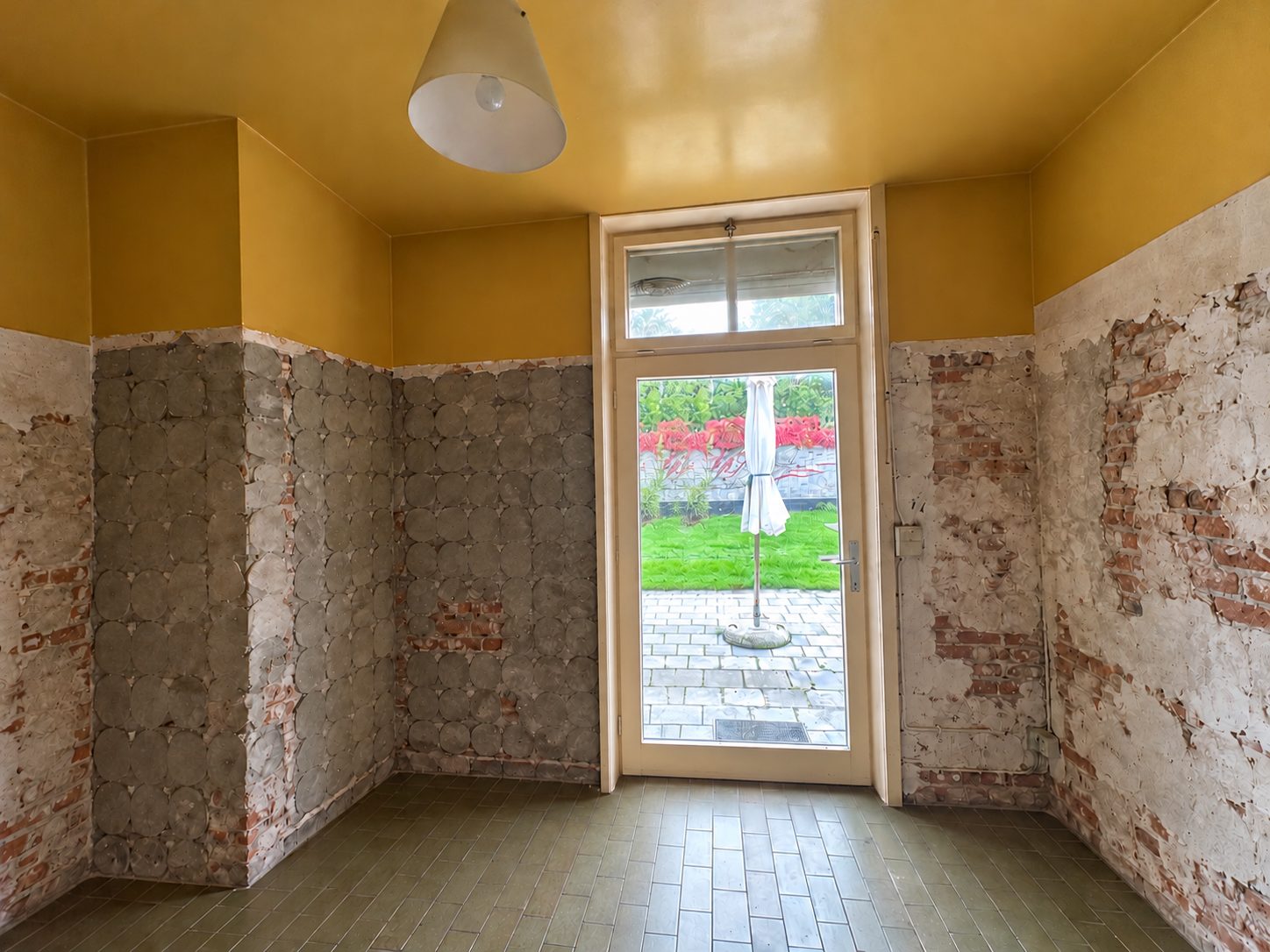 De lege keuken met glazen deur naar de tuin, blote baksteen en gele plafonds