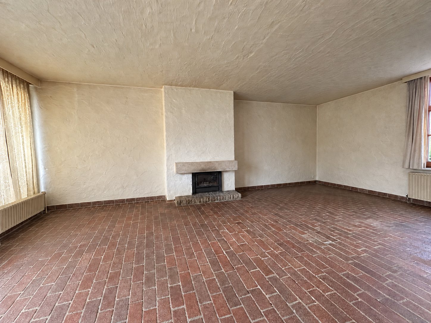 De lege living met haard en baksteenvloer, vanuit dezelfde hoek als het voorstel
