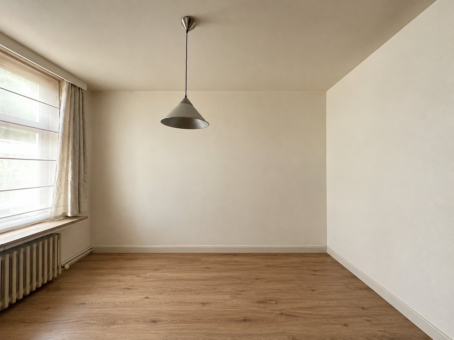 De lege kamer met groot raam en radiator
